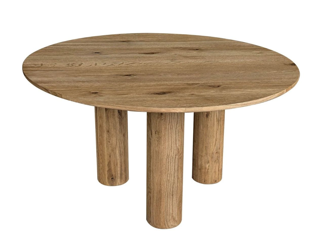 Round wooden dining table with thick pillar legs and upholstered chairs in a neutral dining room.