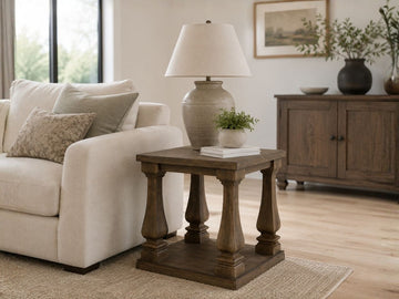 Dark wood end table with turned pedestal-style legs and a lower shelf, styled beside a cream sofa in a warm traditional living room.