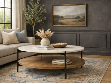 Round coffee table with a light stone top and wood lower shelf in a living room.