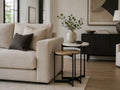 Nested marble and wood side tables beside a cream sofa in a contemporary living room.