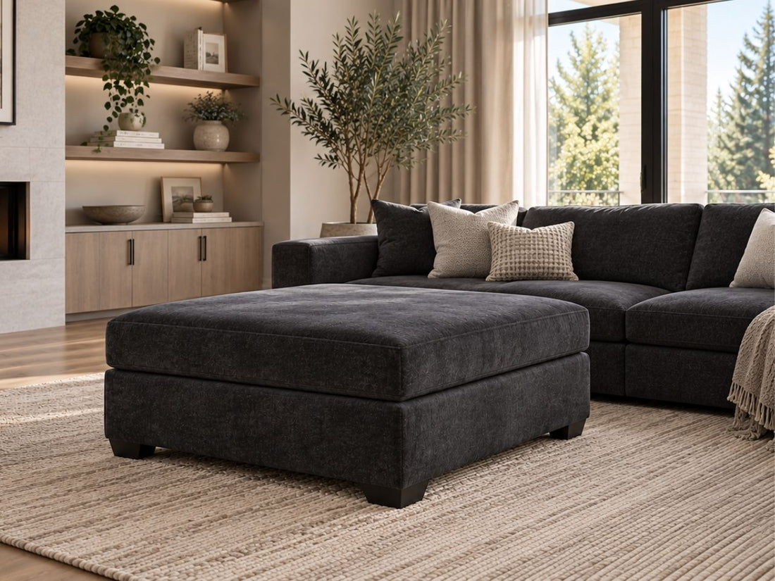 Charcoal upholstered ottoman with matching dark sectional in a luxurious modern living room, featuring warm neutral décor and contemporary furniture in Calgary.