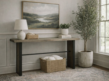 A modern industrial console table with a thick, natural wood top and wide, dark metal slab legs connected by a thin horizontal support bar.