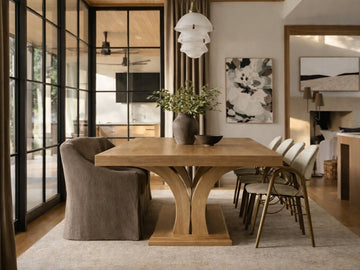 light wood rectangular dining table with upholstered cream chairs, styled in a dining room with a rug. 