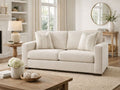Cream upholstered loveseat styled in a bright living room with accent pillows and wood tables.