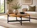 Round tray-top coffee table featuring a natural wood finish and black metal base, styled in a contemporary living room with neutral décor.