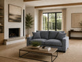 Blue upholstered sofa in a bright modern living room with a fireplace, large windows, wood accents, and a woven area rug