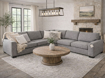 Gray upholstered sectional sofa styled in a spacious living room with a round wood coffee table and fireplace.