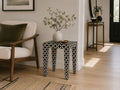 Black and white patterned accent table styled beside a wooden accent chair in a modern living room.