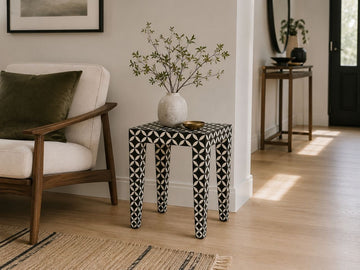 Black and white patterned accent table styled beside a wooden accent chair in a modern living room.