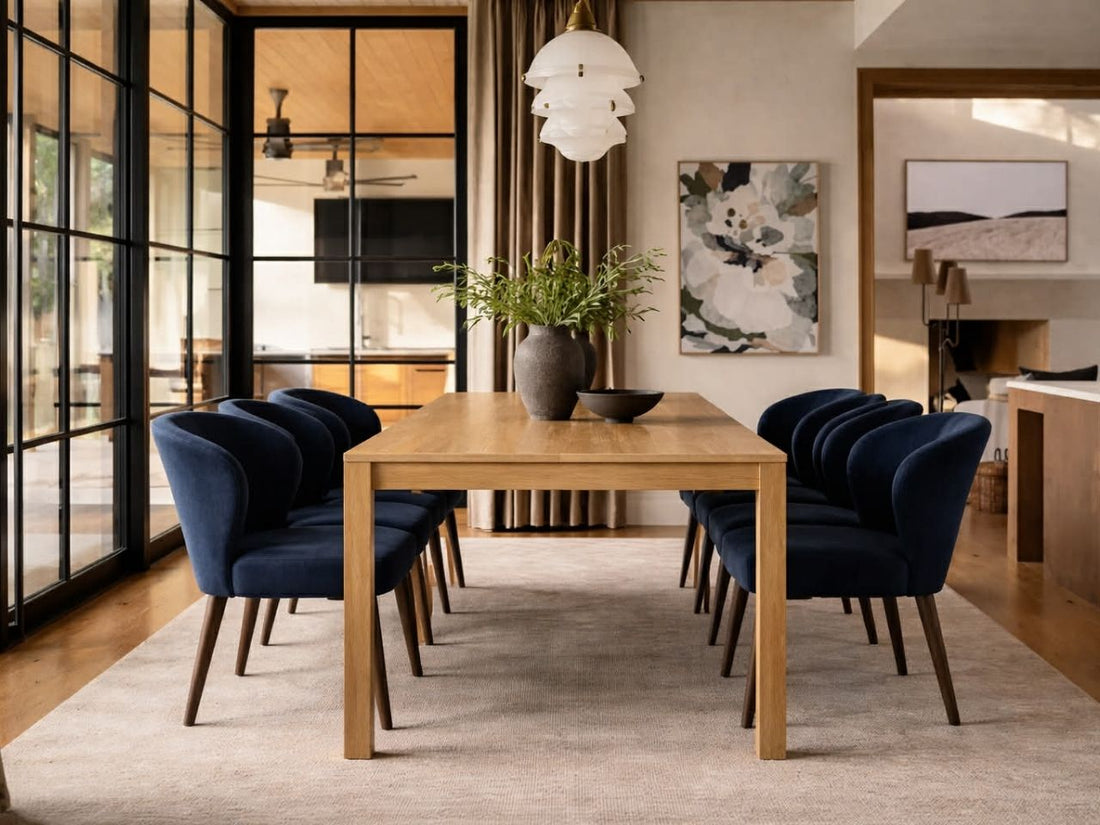 A wooden dining table with navy upholstered chairs, styled in a modern dining room with large glass doors and neutral decor