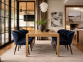A wooden dining table with navy upholstered chairs, styled in a modern dining room with large glass doors and neutral decor