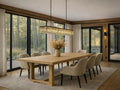 Wood trestle extension dining table with upholstered chairs in a warm, modern dining room with large windows.