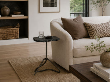 Black slate accent table with an organic stone top and sculptural metal base, styled beside a cream sofa in a modern living room.