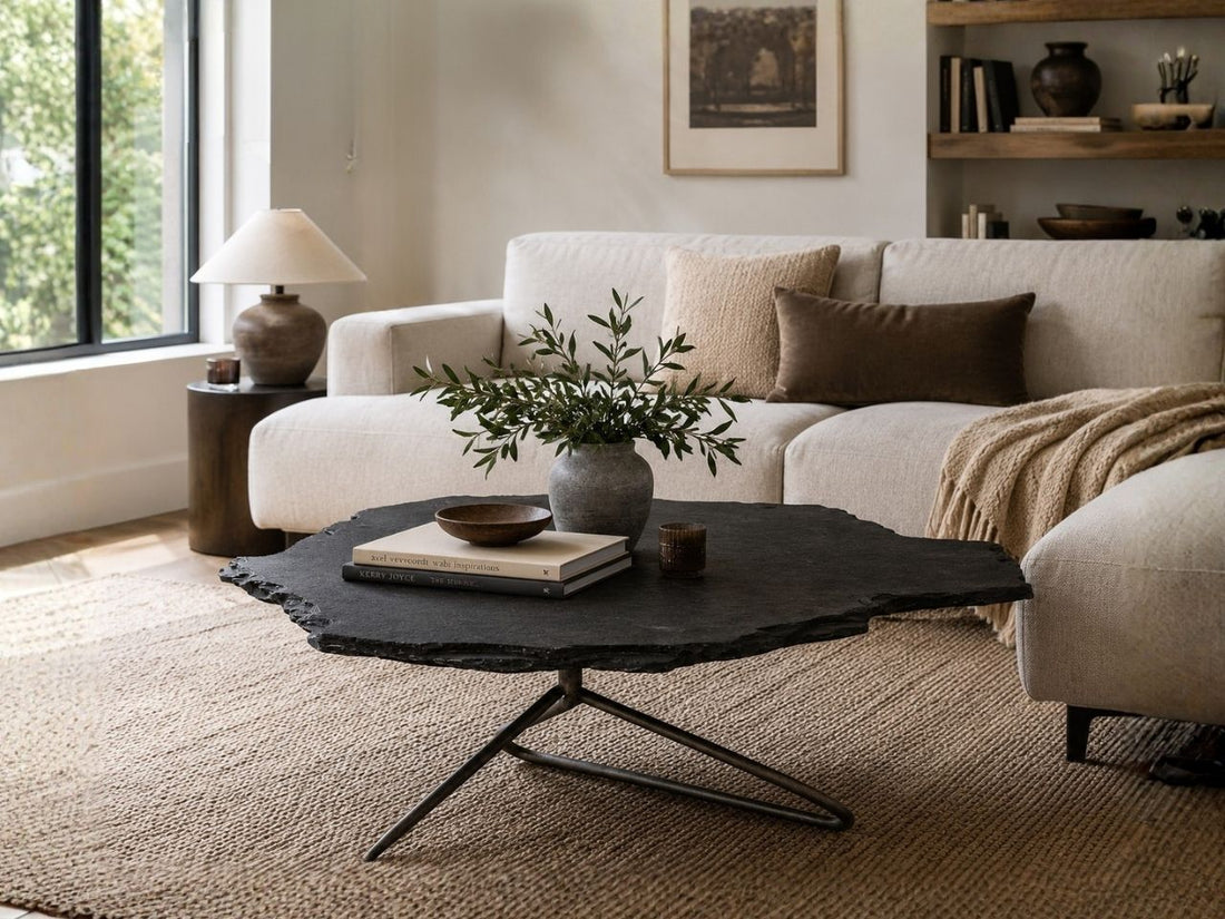 Black organic-shaped coffee table with a metal base, styled in a cozy living room with a cream sofa, textured rug, and decorative accents.
