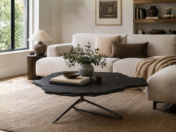Black organic-shaped coffee table with a metal base, styled in a cozy living room with a cream sofa, textured rug, and decorative accents.