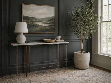 A slim console table with a white marble top and a thin antique gold-finished metal frame. 