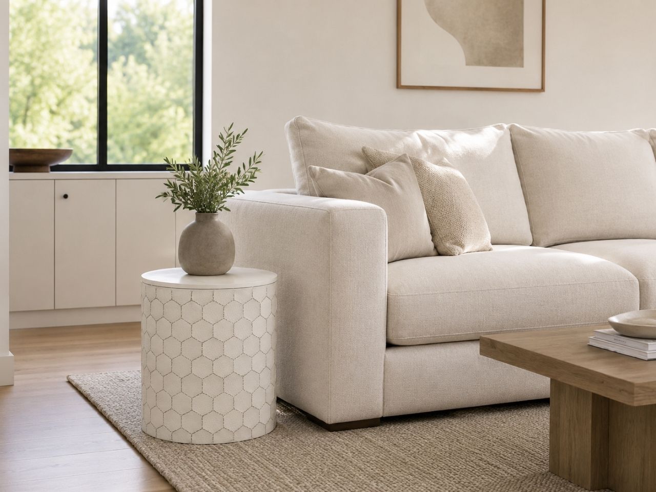 White cylindrical side table with a subtle geometric pattern, styled beside a cream sofa in a bright, modern living room.