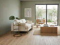 Round metal accent table with a bronze finish and glass top, styled beside a cream sofa in a bright modern living room.