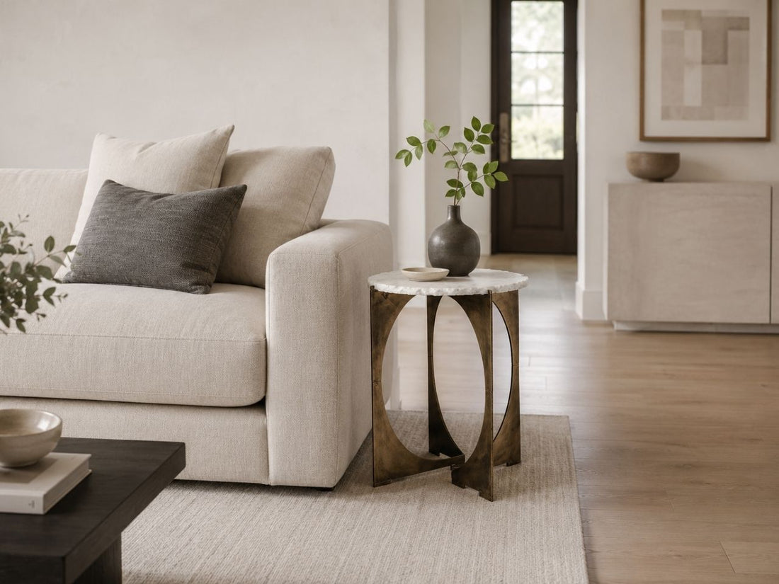Round marble side table with a metal base beside a cream sofa.