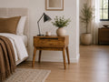 Mid-century solid wood nightstand with a drawer styled beside a neutral upholstered bed in a warm modern bedroom.