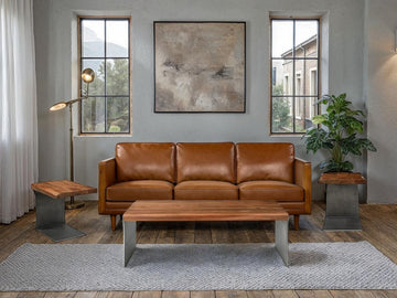 A styled living room featuring a leather sofa with wood arms, a rectangular wood-and-metal coffee table centered on a textured area rug, and matching side tables.