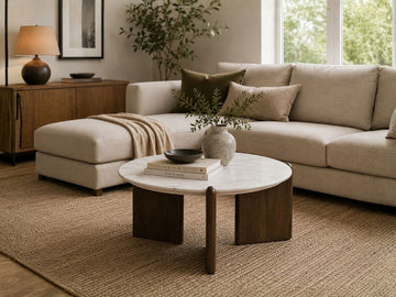 Round coffee table with a white marble top and dark wood base in a cozy living room.