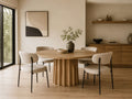 Modern round wood dining table with upholstered chairs in a bright contemporary dining room.