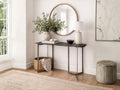 A slim, minimalist console table featuring a live-edge black stone or textured dark wood top supported by a thin, dark bronze metal frame with a unique three-leg geometric base.