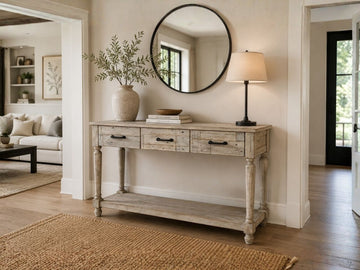 Rustic farmhouse console table with drawers and lower shelf styled with a round mirror, lamp, and neutral décor.