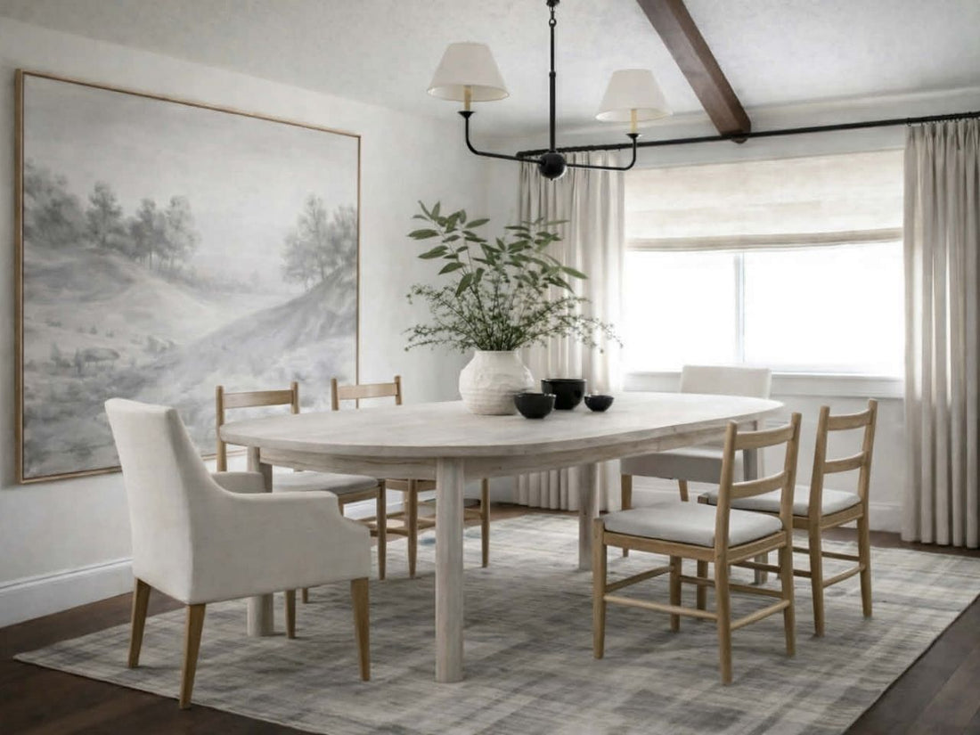 Light wood oval dining table with pedestal legs and mixed dining chairs in a bright, neutral dining room.