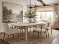 Light wood oval dining table with six upholstered chairs in a bright dining room.
