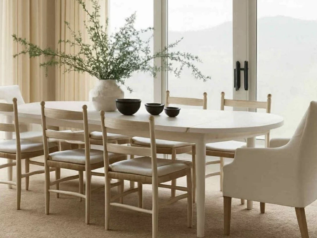 Oval-shaped piece table made of light-toned solid wood surrounded by a set of matching light wood dining chairs.