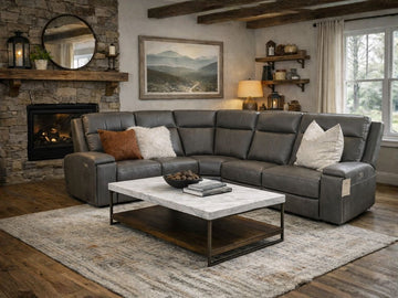 A gray leather sectional sofa styled in a warm, rustic living room with a stone fireplace.