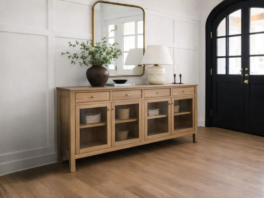 Light wood sideboard with glass-front cabinet doors and storage drawers, styled in a bright entryway with modern décor and a large wall mirror.