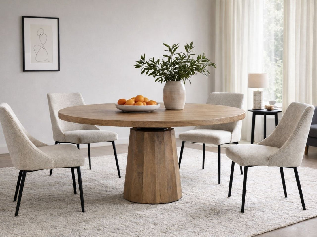 Light wood round dining table with pedestal base and upholstered chairs in a bright dining room.