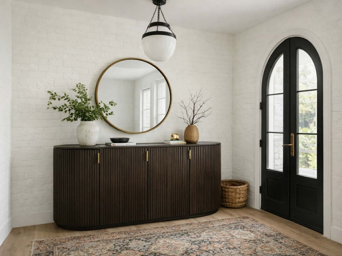 A dark brown, oval-shaped sideboard with a vertical fluted texture and gold handles sits against a white brick wall.