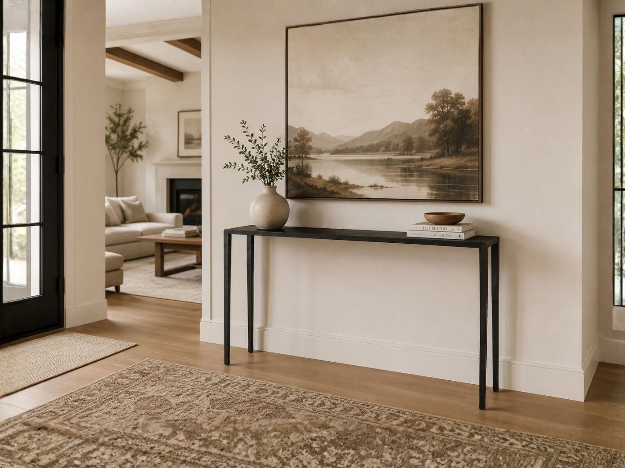 Minimalist black console table styled beneath a large landscape artwork in a warm, modern hallway.