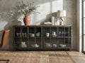 A low, industrial-style sideboard with a dark metal frame and glass-paneled doors sits against a textured concrete wall.