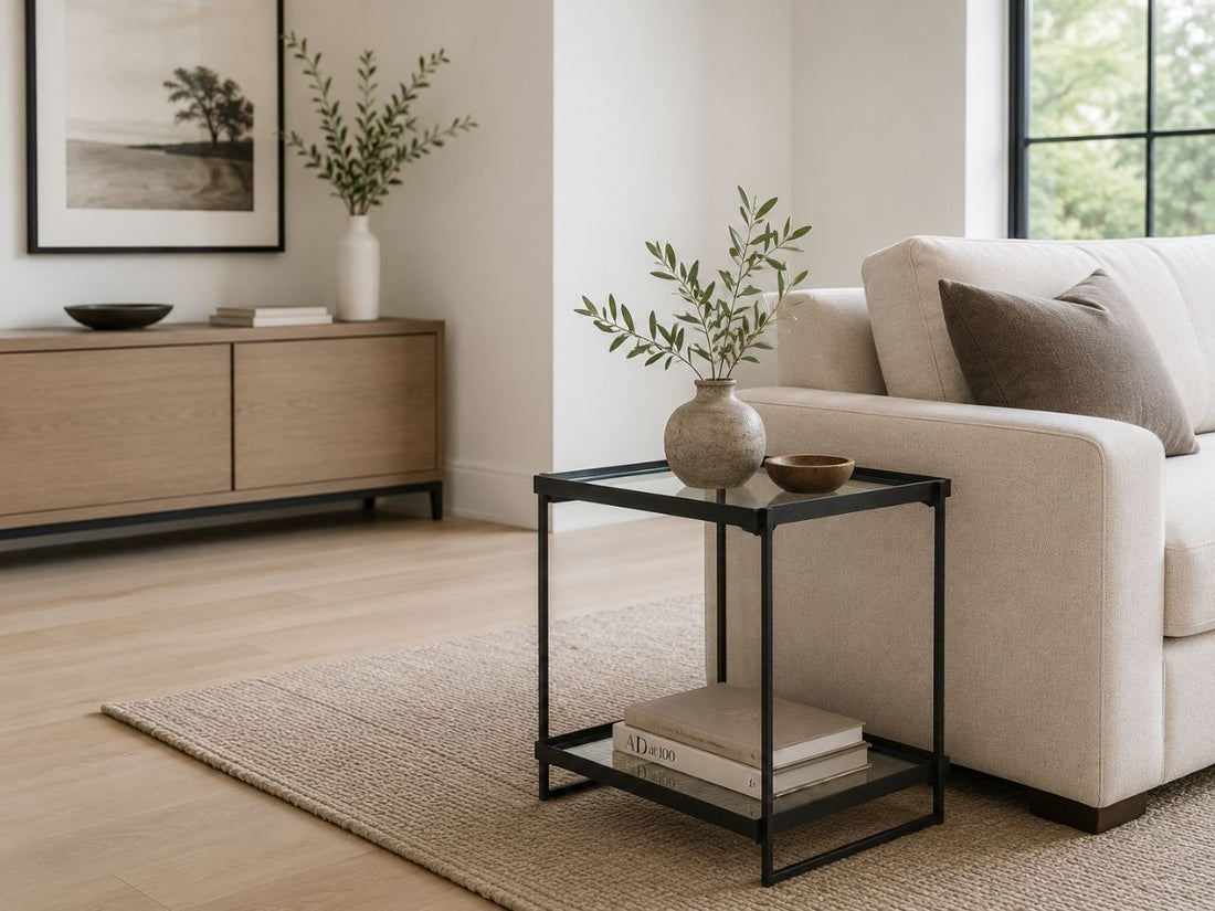 Modern black metal and glass accent table with a lower shelf, styled beside a cream sofa in a bright contemporary living room.