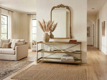 Gold metal console table with open shelves styled in a bright entryway.