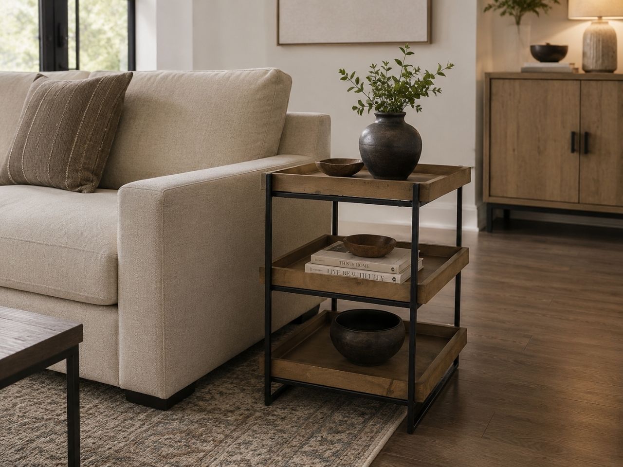 Rustic wood and black metal side table with three open shelves styled beside a cream sofa in a warm modern livingroom.