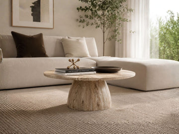Round wood coffee table with a pedestal base styled in a cozy living room with a sectional sofa.