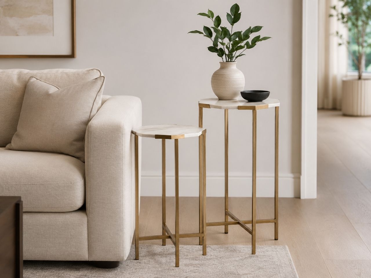 Marble top nesting side tables with gold metal frames beside a cream sofa.