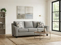Light gray sofa in a modern living room with a round coffee table, abstract wall art, and large window.