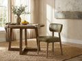 Sage green leather dining chair with wood legs beside a round wood table in a bright dining room.