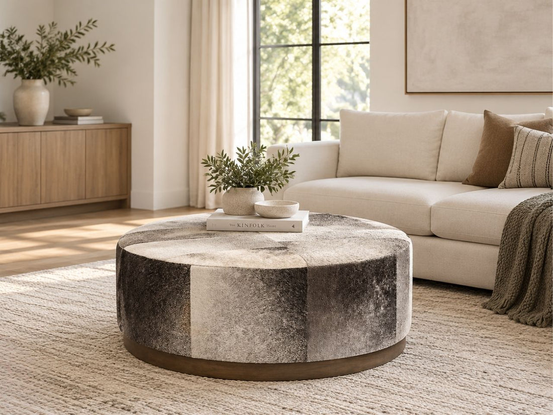 Round patchwork ottoman in neutral cream, beige, and brown tones with a dark wood base, styled as a modern ottoman in a Calgary living room.